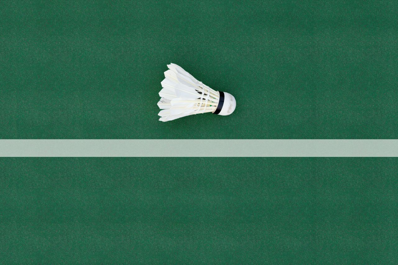 hero-img-01 A shuttlecock lies on a green badminton court floor, highlighting sports simplicity.
