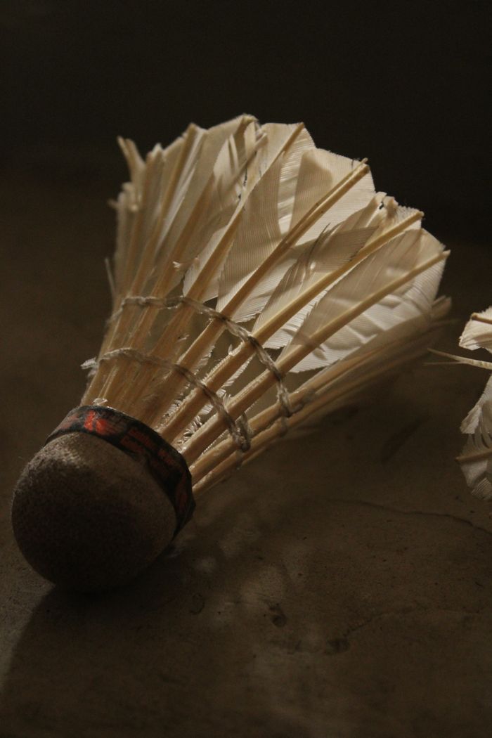 Detailed view of a badminton racket lying on a wooden floor with focused strings, perfect for sports-related themes.
